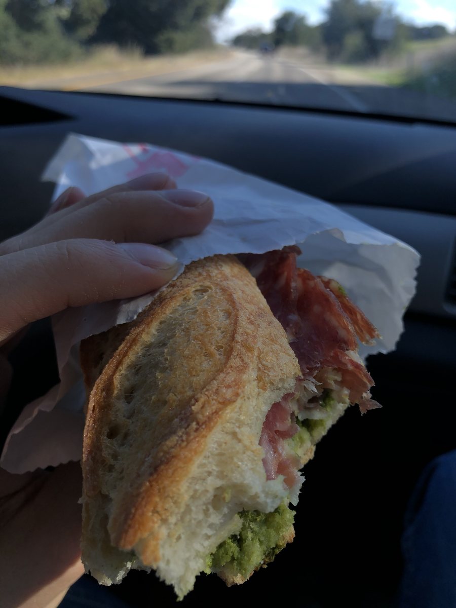 1:30 PM Jonah took this beautiful photo of the baguette sandwich he was feeding me as I drove us home, with charcuterie, cheese, butter, and pesto on it!